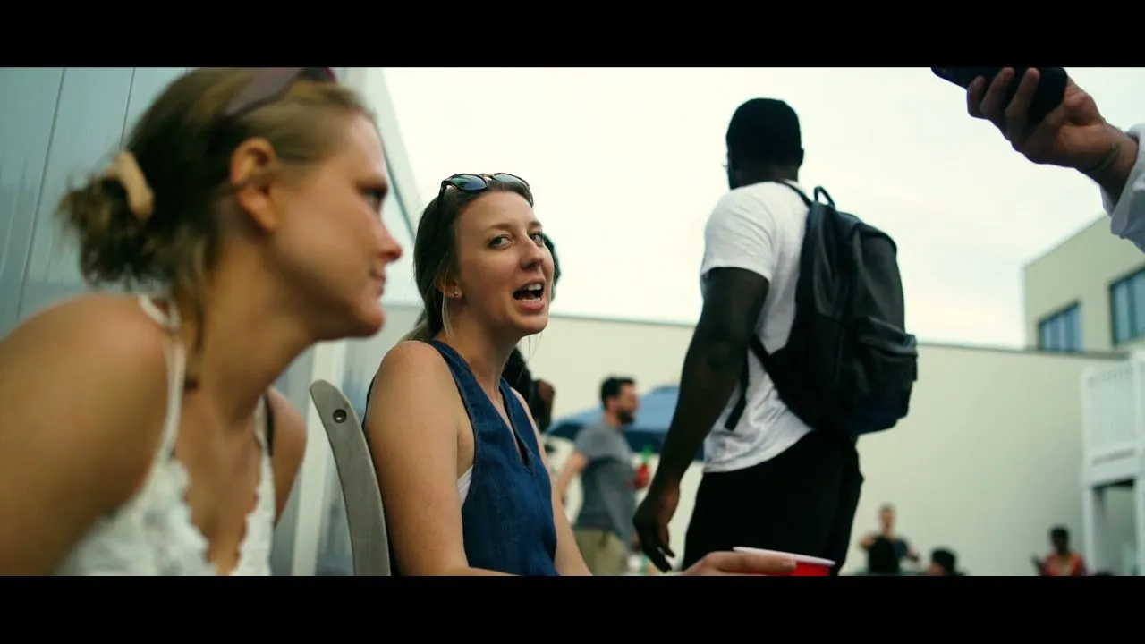 Two people talking at crowded outdoor rooftop party in daylight