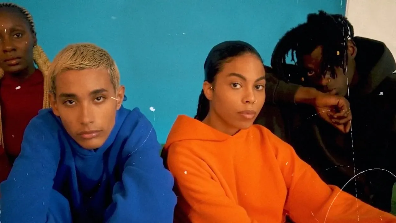 Two people in blue and orange sweatshirts against teal background, seated indoors