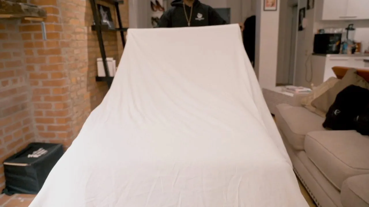 White-sheeted massage table in dim room with exposed brick wall