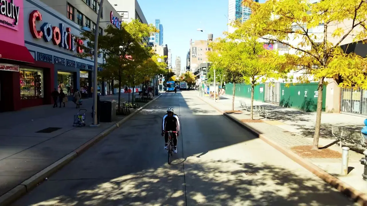 Cyclist riding down empty city street lined with storefronts, daytime