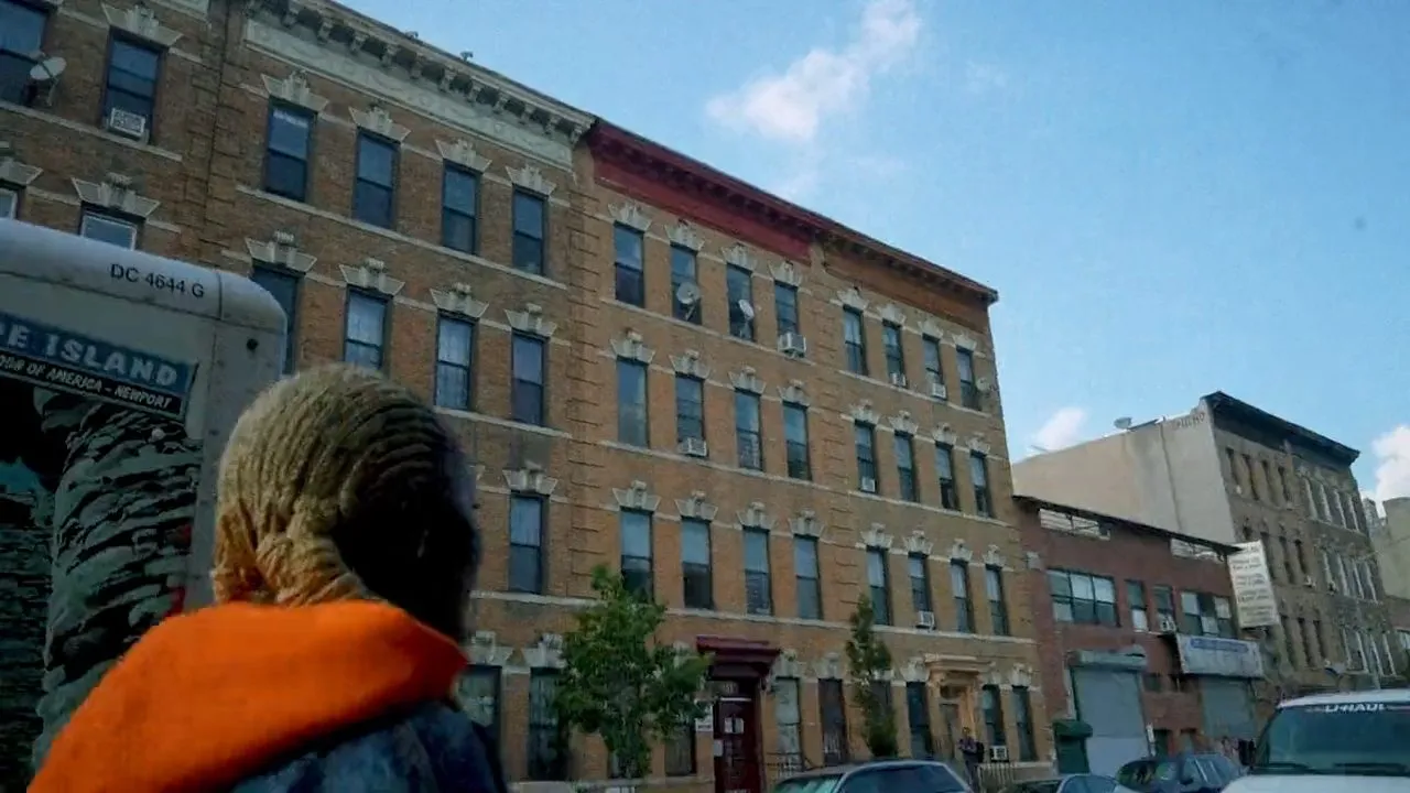 Person in orange hoodie facing brick apartment buildings under blue sky