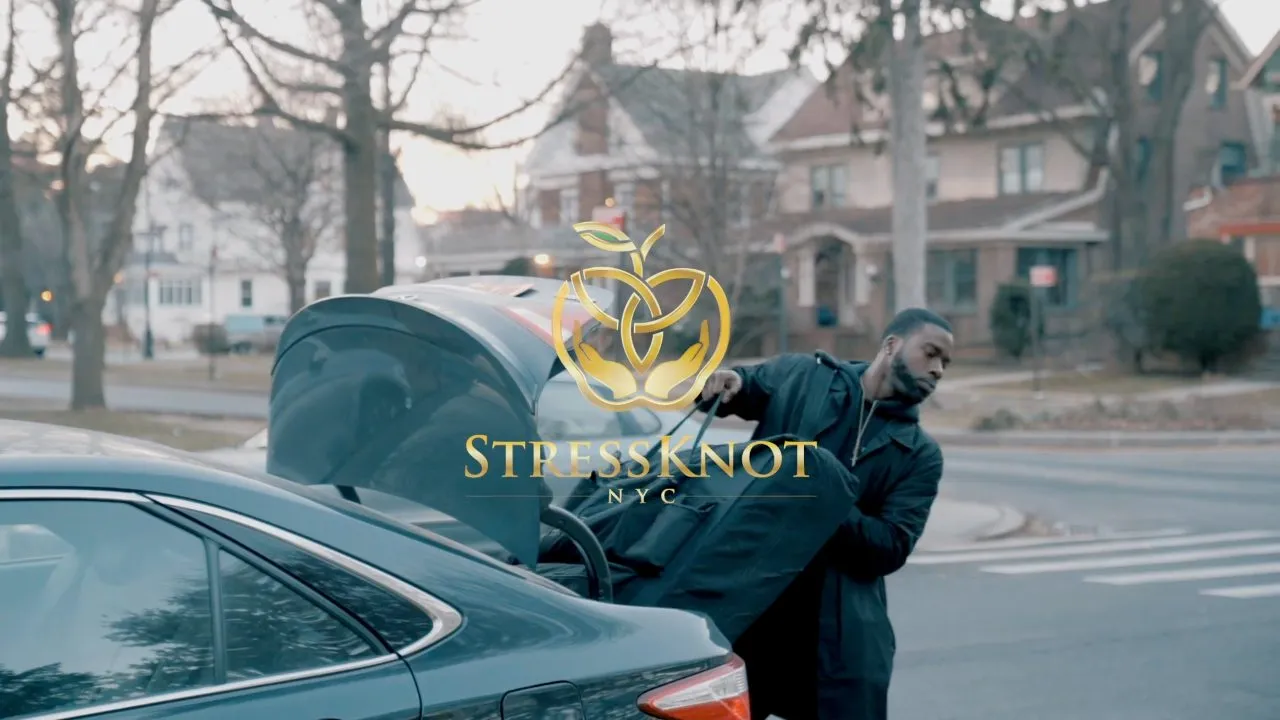 Person at open car trunk on residential street, StressKnot NYC logo overlay