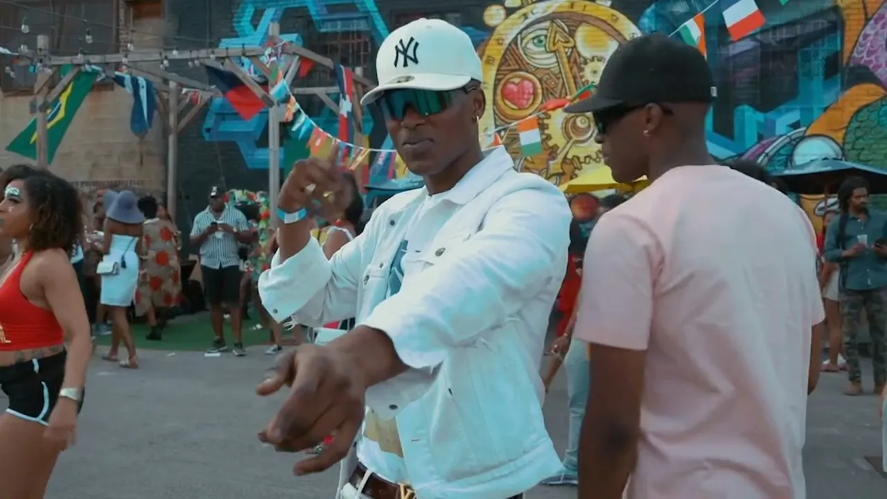 Person in white denim jacket and cap outdoors before colorful graffiti wall