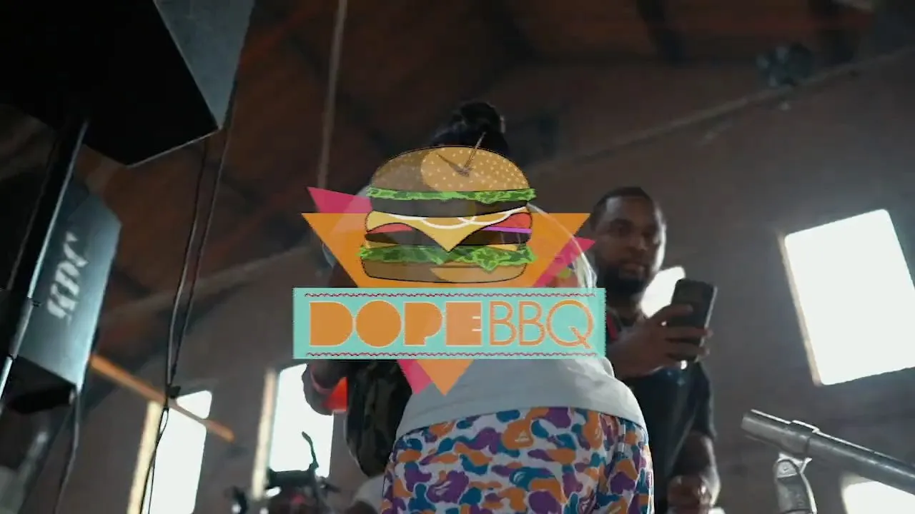 Person holding phone beside colorful DOPE BBQ burger logo graphic in industrial venue