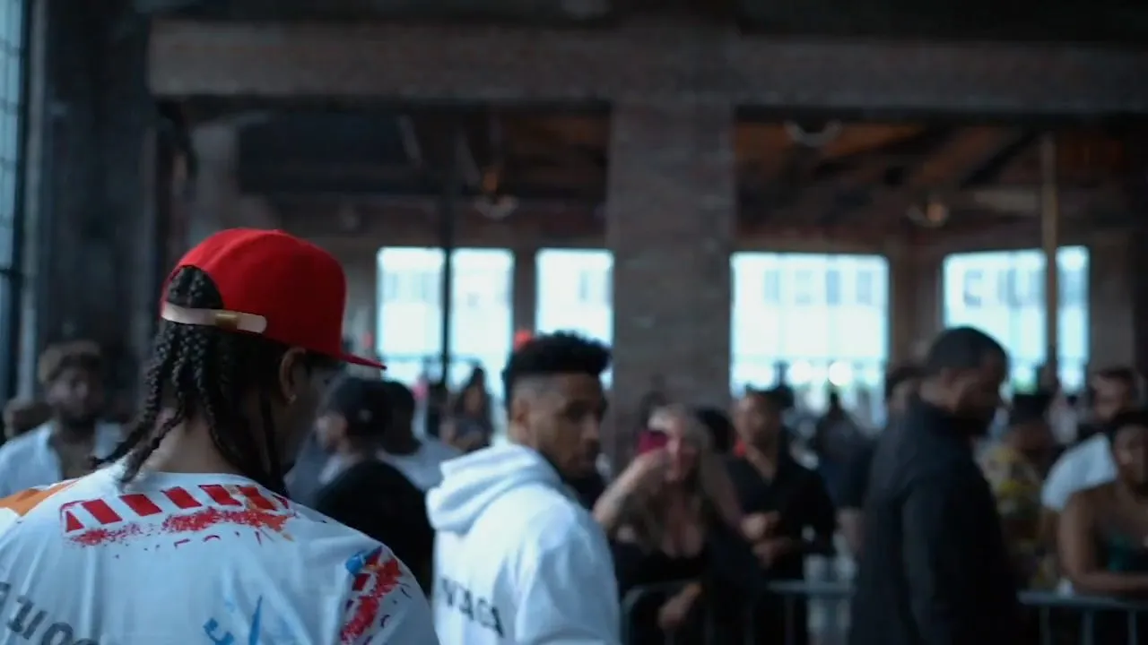Crowd in hoodies gathered in brick warehouse space with bright windows