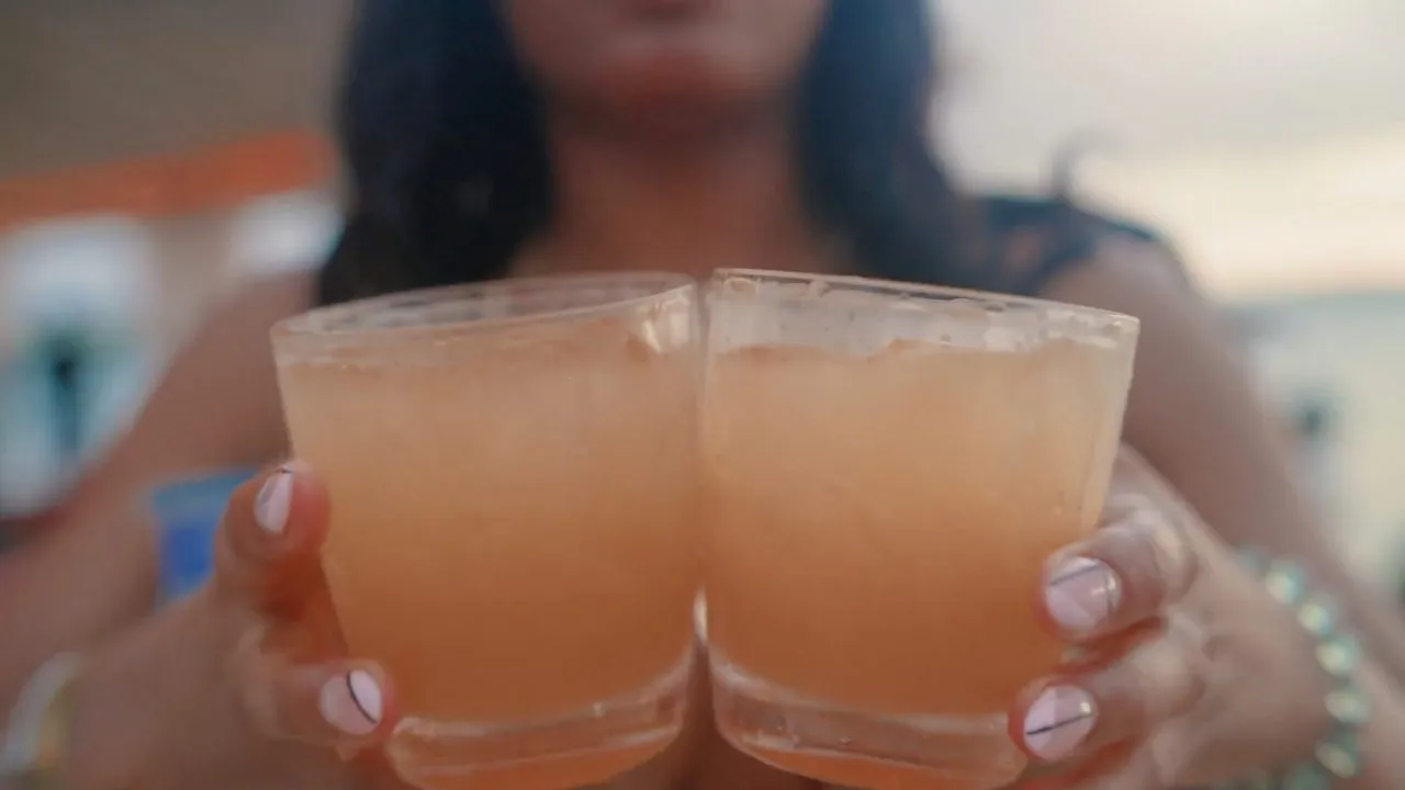 Two hands toasting cocktail drinks in clear cups, close-up