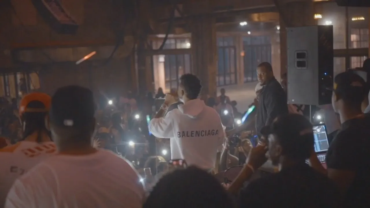 Crowd raising phones toward performer near speaker stack in dim venue