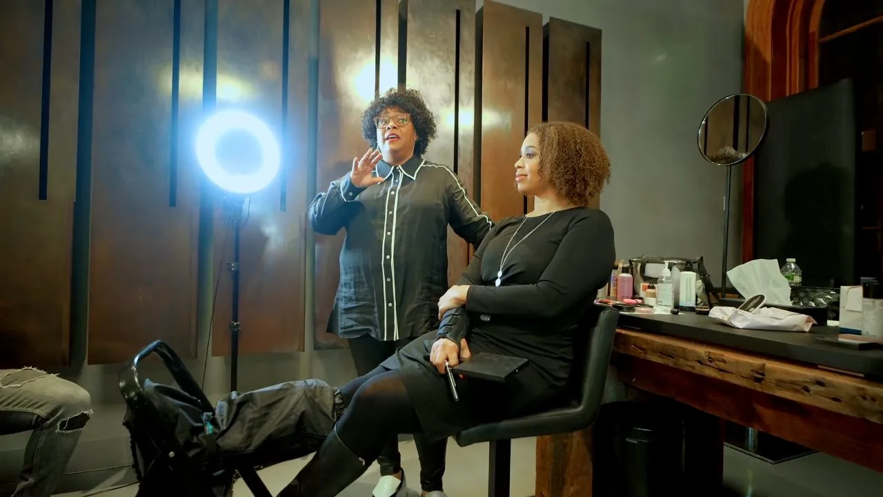 Person seated at makeup station near ring light in dim store