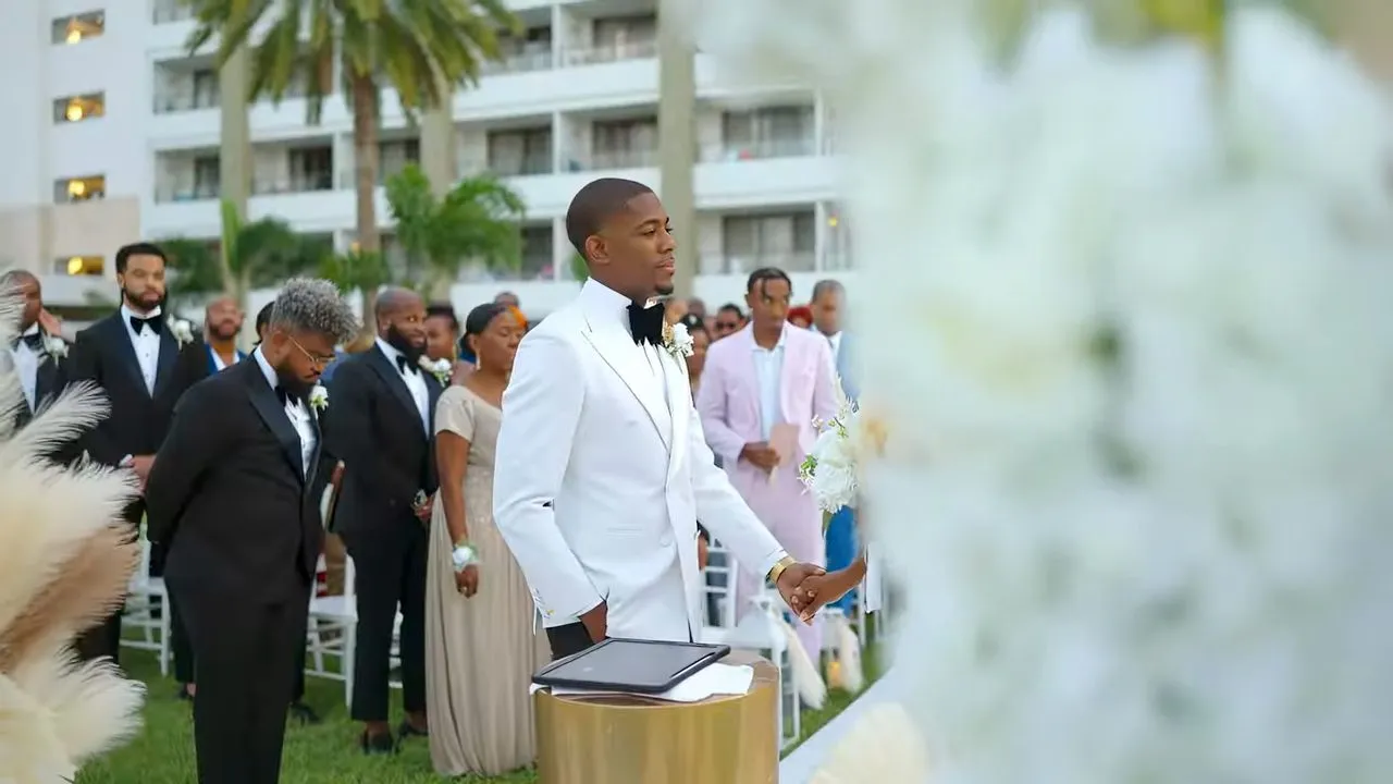 Outdoor beachside wedding ceremony, guests in tuxedos beside palm trees and hotel
