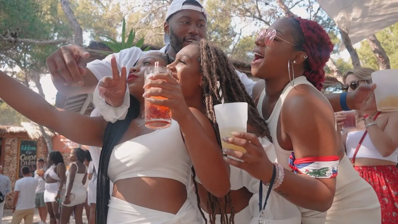 People in white outfits dancing with drinks at outdoor party