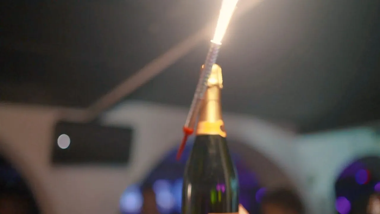 Champagne bottle with sparkler lit at dim indoor party venue