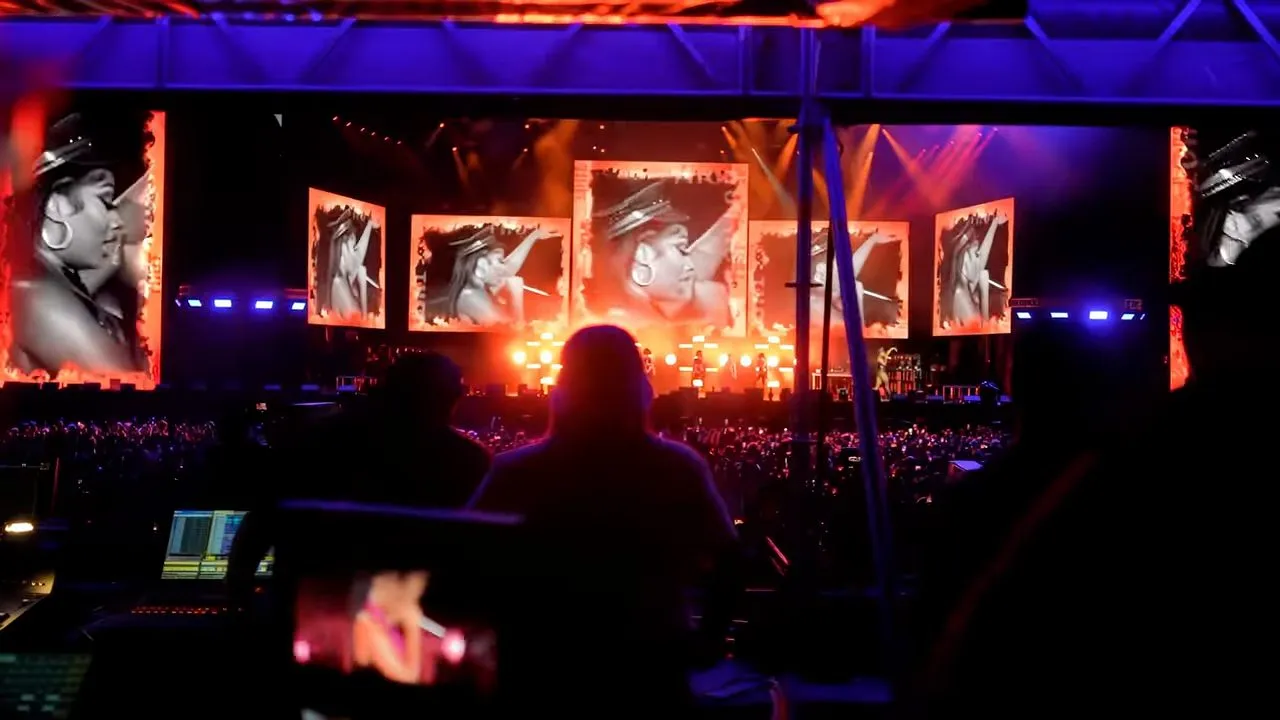 Large concert stage with screens, dramatic lighting, silhouetted performer at night