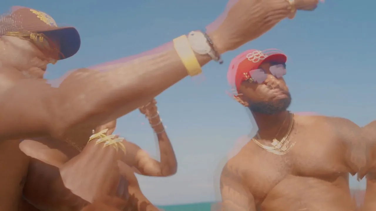 Shirtless man in red cap raising arm on beach, bright sky