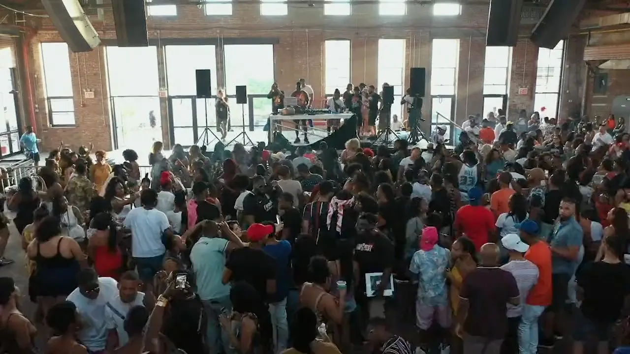 Large dense crowd gathered facing a stage inside brick warehouse venue