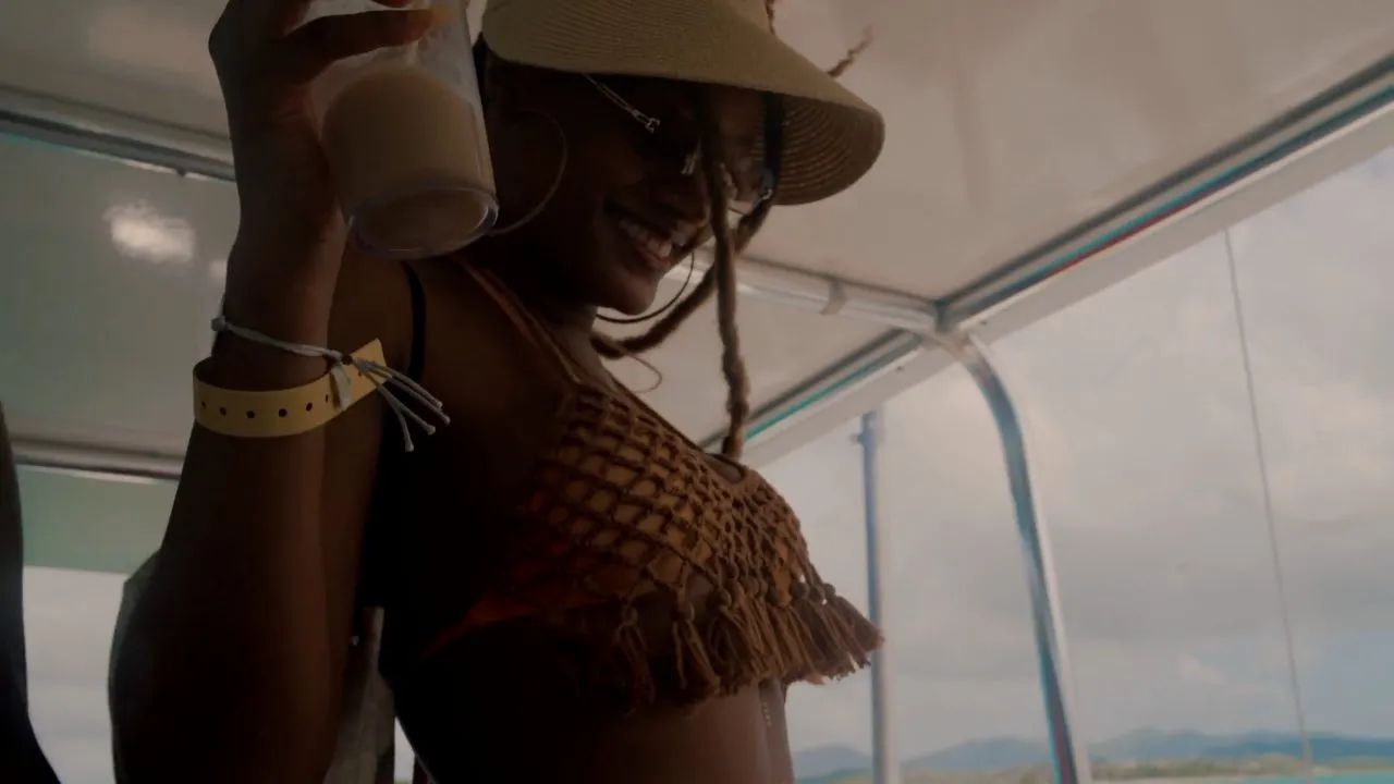 Person in sun hat drinking from cup on boat, coastline behind
