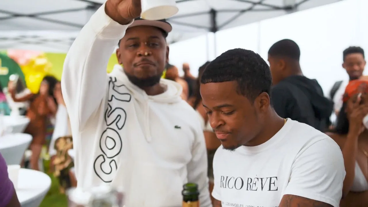 Men in white shirts under tent at outdoor gathering, bottles on table