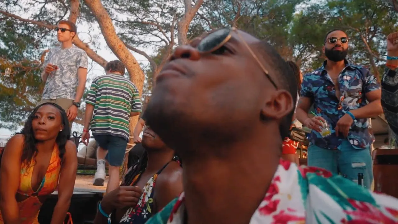 Person in floral shirt and sunglasses looking up outdoors, crowd behind