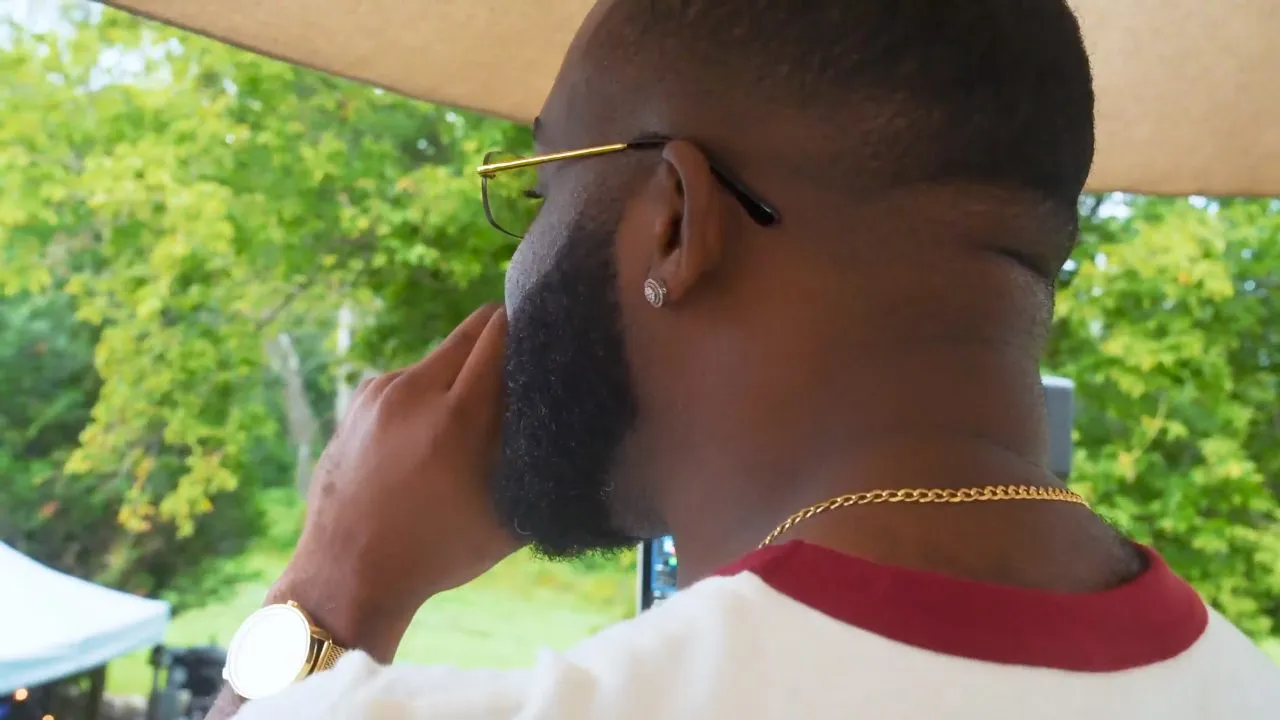 Close-up back of man's head with beard, gold chain, outdoor greenery