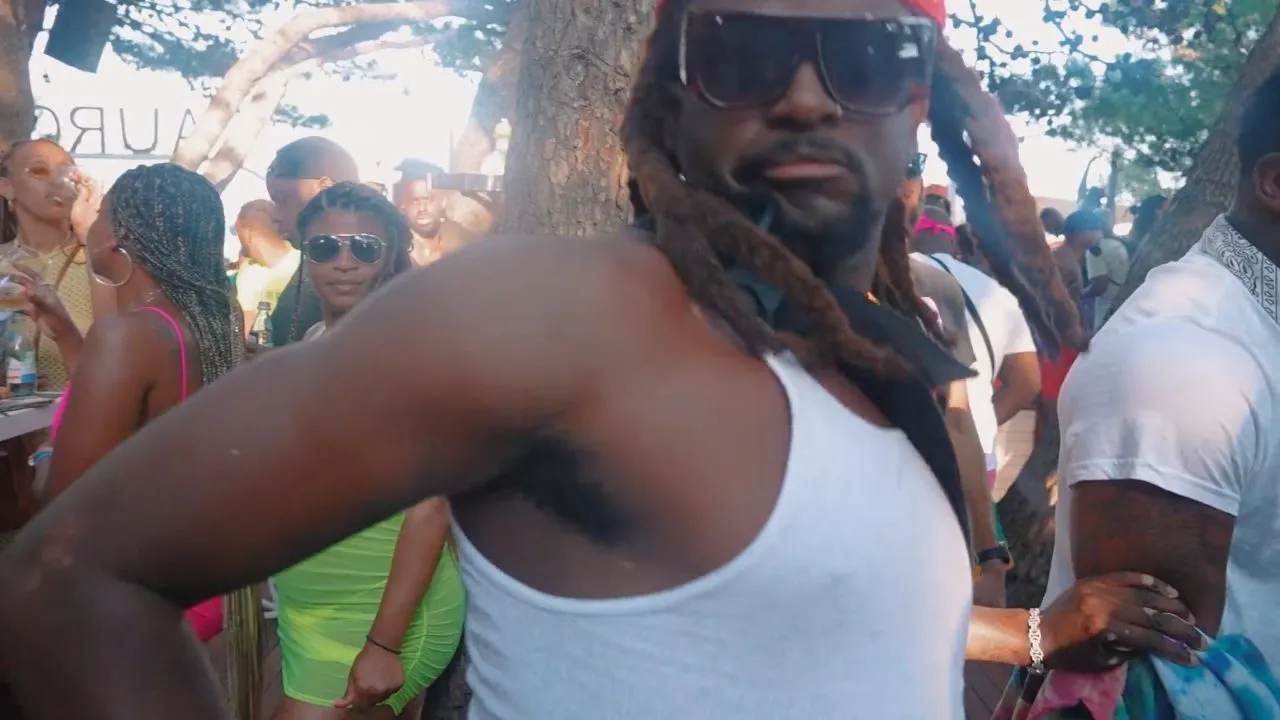 Person in white tank top and sunglasses dancing in daytime crowd