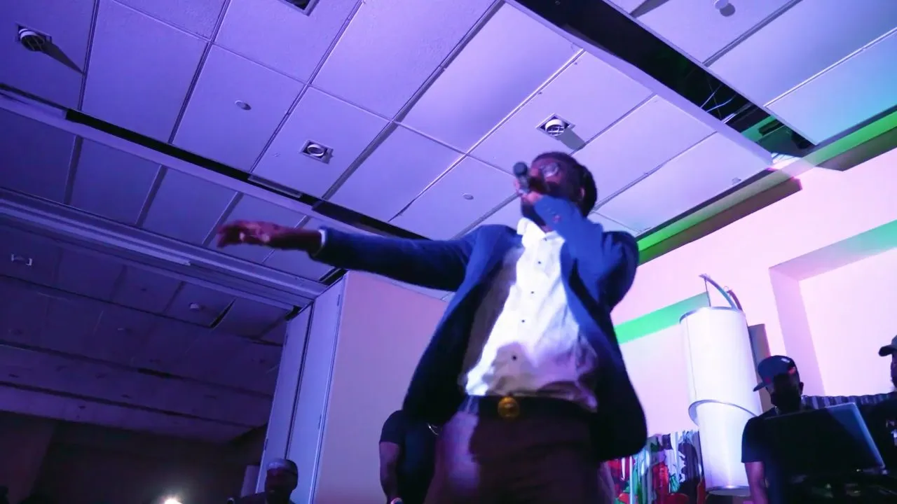 Man in dark jacket and white shirt performing on dim event floor