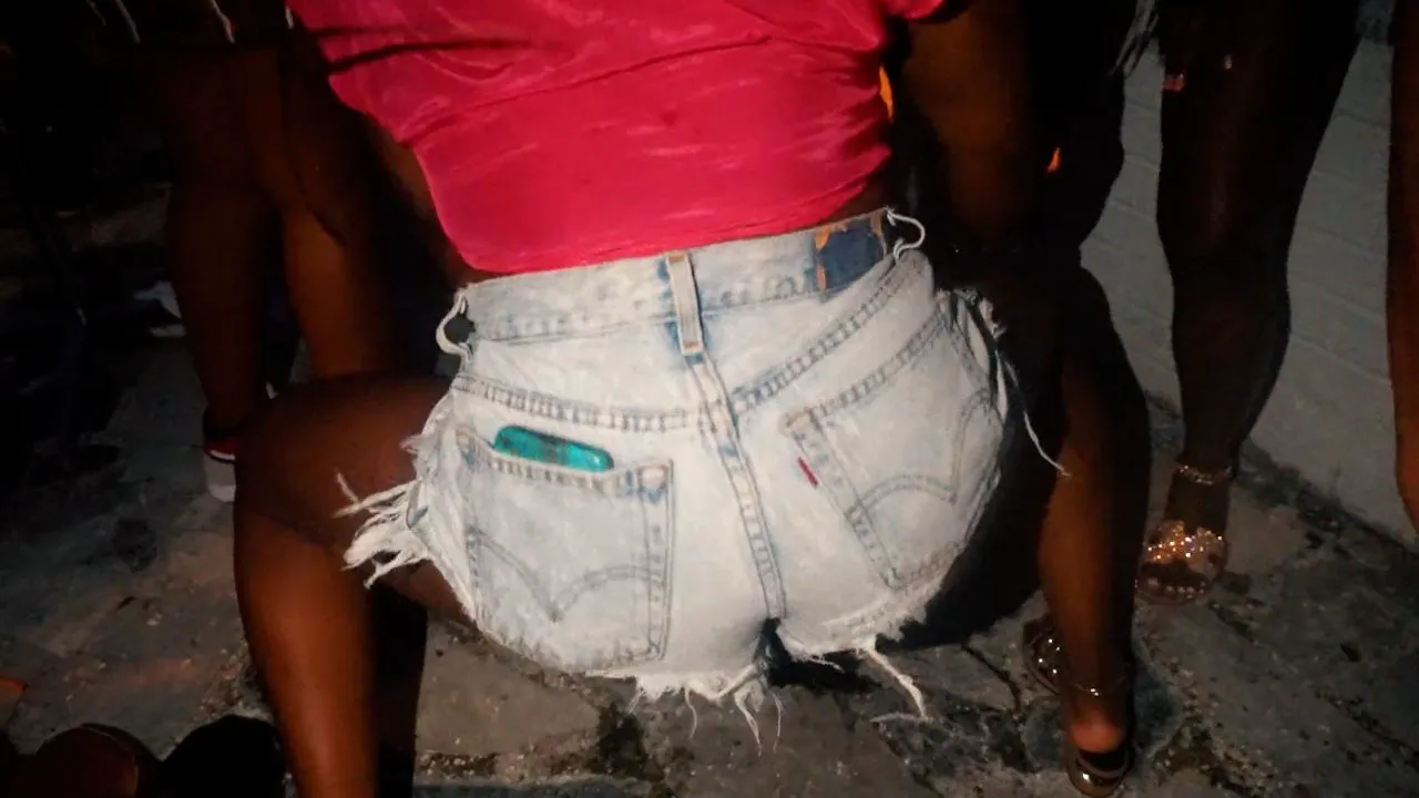Person in denim shorts dancing on dirt at outdoor backyard party, daytime