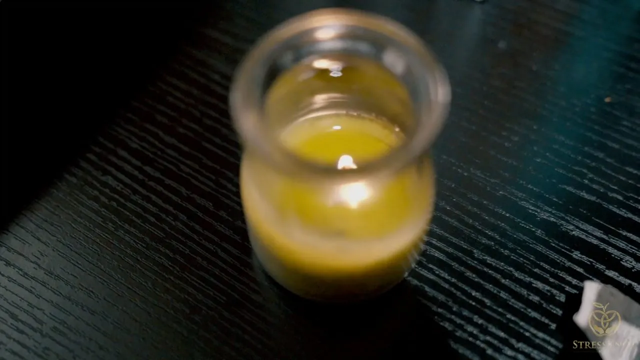 Lit yellow candle in glass jar on dark surface, warm glow