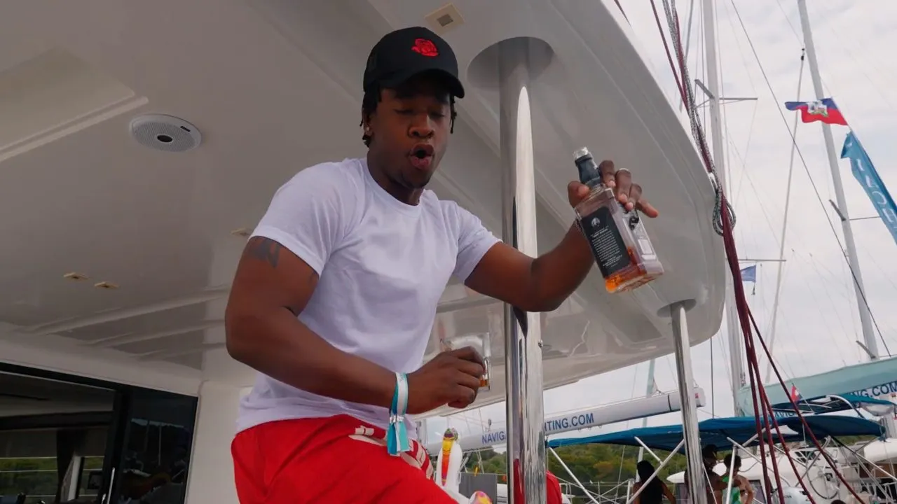 Person in white tee and cap holding bottle aboard a yacht