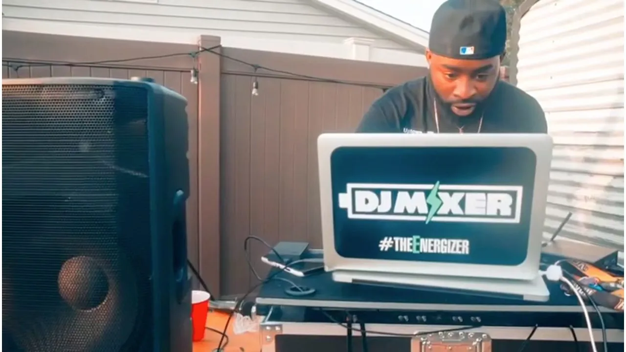 DJ at outdoor setup with speaker and DJ Mixer branded laptop, daytime