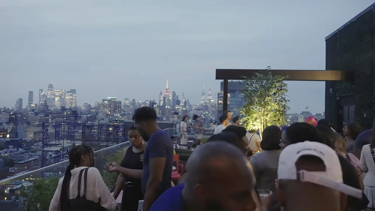 Rooftop gathering at dusk overlooking city skyline, people socializing