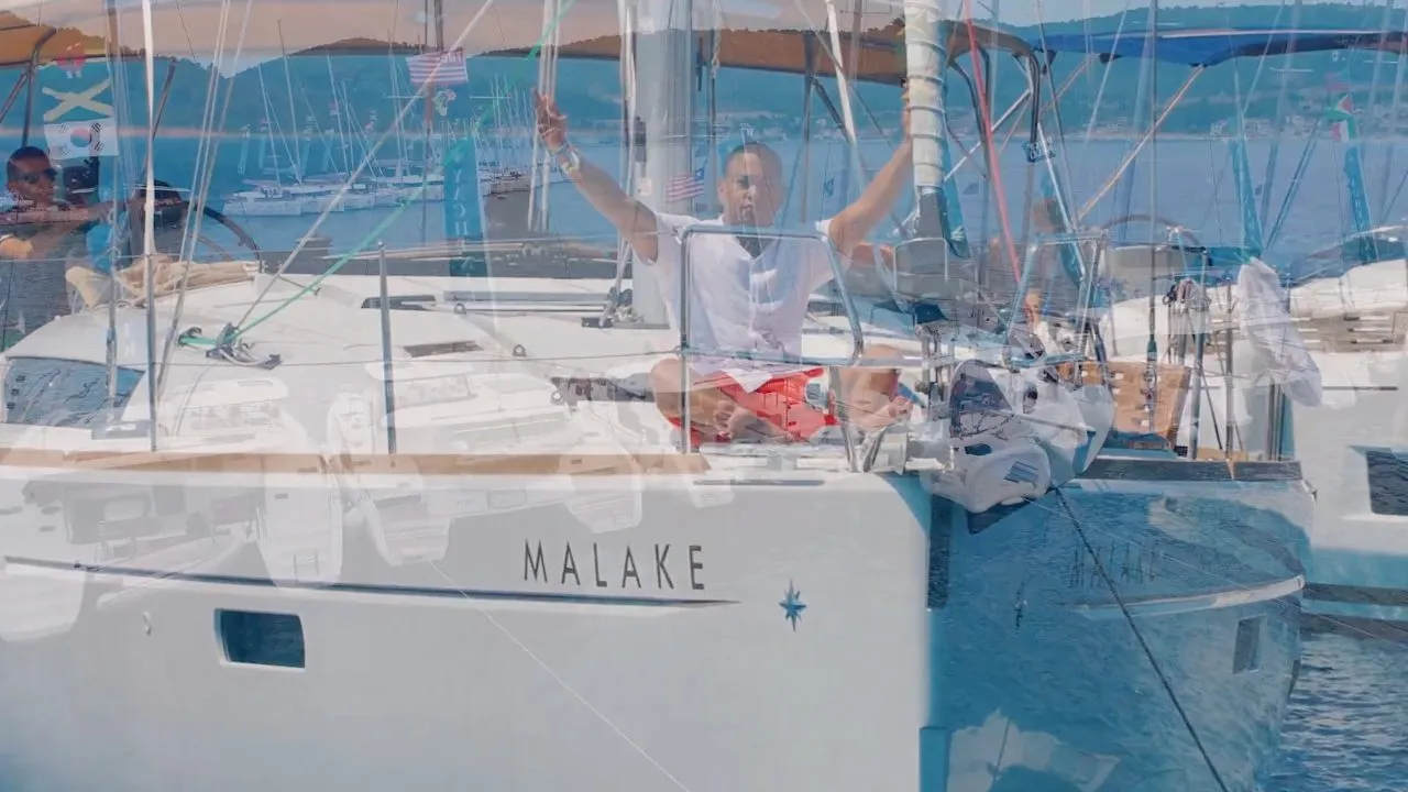 White catamaran named MALAKE moored in calm harbor water, daylight