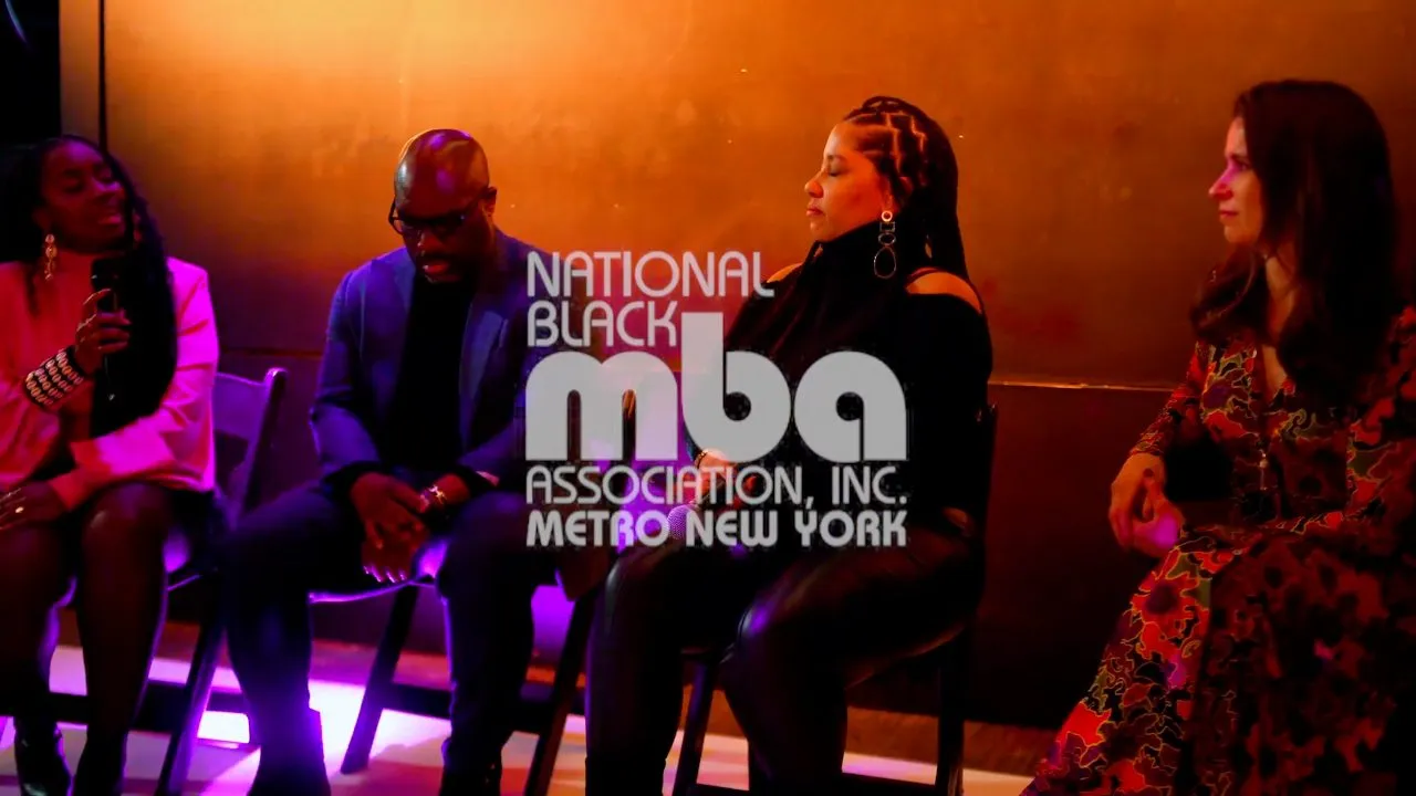 Panelists seated on stage beside National Black MBA Association Metro New York logo, dim lighting