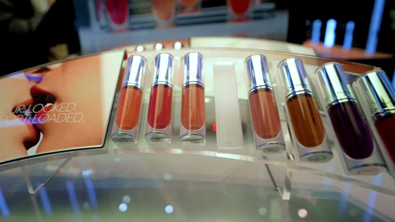 Row of colorful lip gloss tubes displayed on glossy counter with lighting
