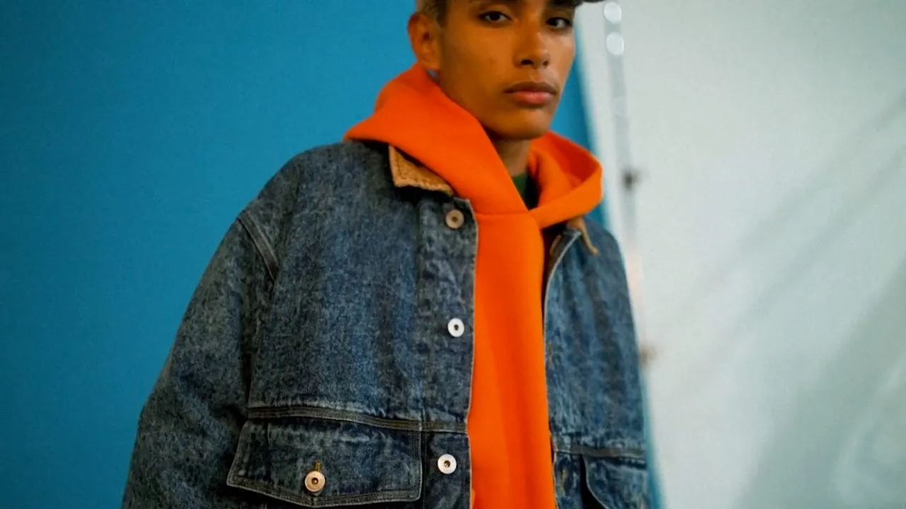 Close-up of denim jacket over bright orange hoodie against light blue background