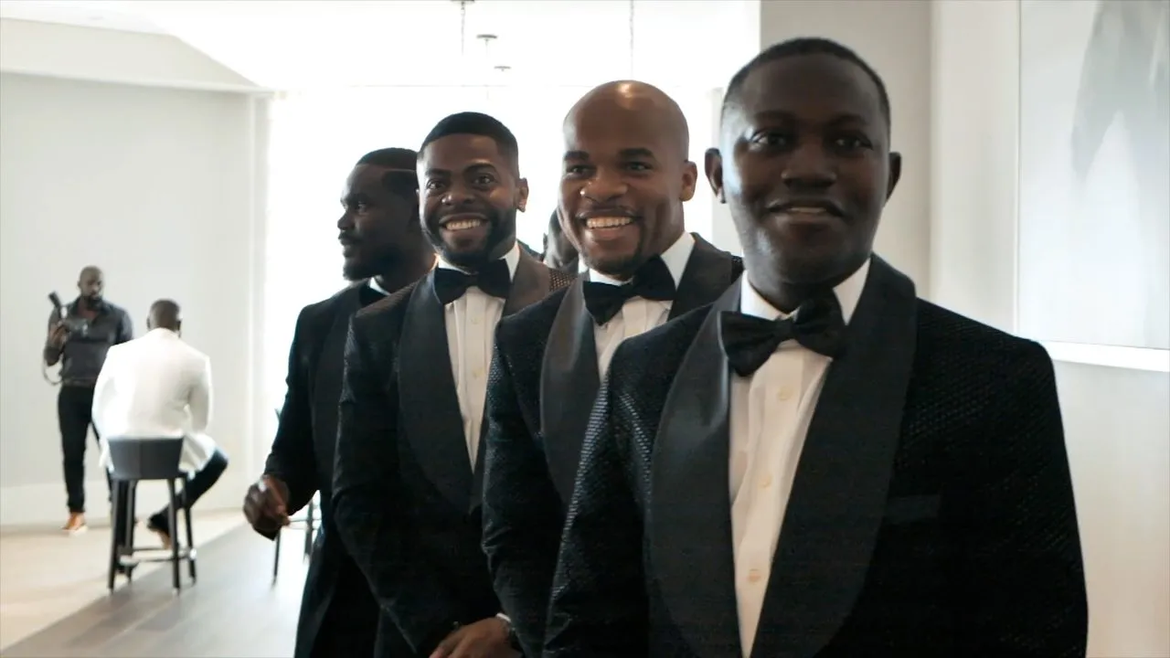 Group of men in black tuxedos and bow ties posing indoors in hallway