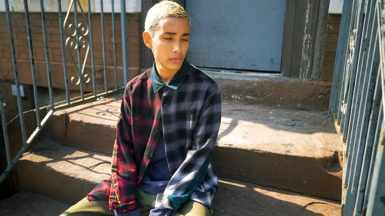 Person in plaid flannel shirt sitting on outdoor stone steps, sunlit