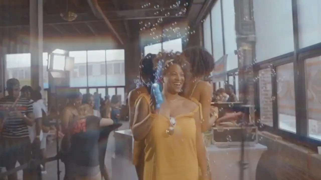 Two smiling women in yellow dress standing among crowd near bright windows
