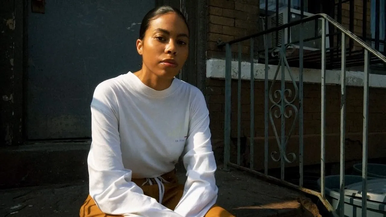 Person in white sweatshirt sitting on stoop by iron railing, sunlit