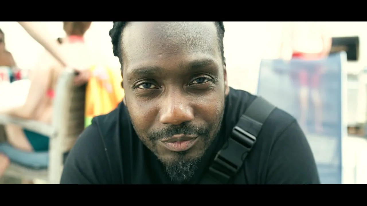 Man with beard looking at camera outdoors, backpack strap visible