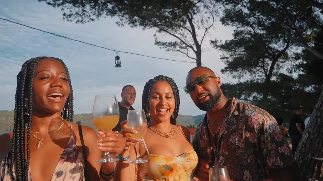 Three people holding cocktail glasses smiling outdoors under trees